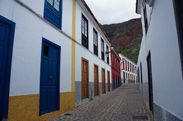 Cobblestone street between white houses with colored windows and doors in the old town of Agulo on the island of La Gomera