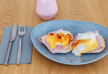 Breakfast plate with two pieces of bread toast topped with ham and fried egg. Also a strawberry milkshake to pair with the food.