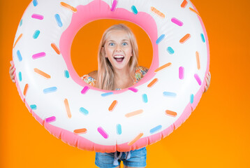 Studio portrait of a blonde girl with a giant colored doughnut with an expression of surprise