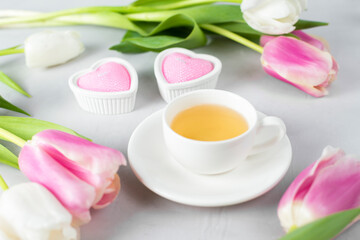 Tulips with white cup of tea on a light background. Spring tenderness still life composition with candles. Flowers for romantic, love atmosphere. Relax, meditation pause. Selective focus, copy space.