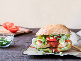 Burger with chicken, tomato, cheese, herbs on the table. 