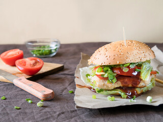 Burger with chicken, tomato, cheese, herbs on the table. 