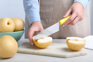Woman cutting ripe apple pear at table, closeup