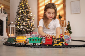 Little girl playing with colorful train toy in room decorated for Christmas