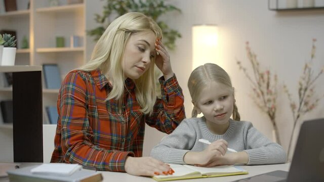 Blond mother feeling tired, trying to help daughter with homework, parenting