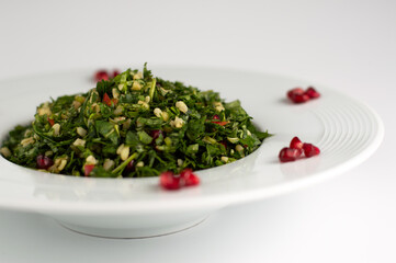 Blurred image of a salad with herbs and bulgur, pomegranate on a white plate on a light background.