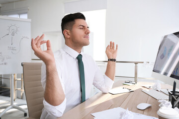 Businessman meditating at workplace in office. Stress relieving exercise
