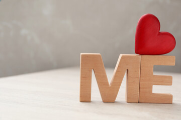 Phrase Love Me made of red heart and wooden letters on white table, closeup. Space for text