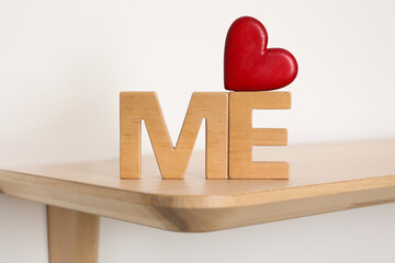 Phrase Love Me made of red heart and wooden letters on shelf, closeup