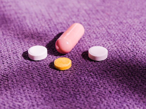 A pink capsule and three round tablets lie on a violet vilvet surface. Photo with linear blur