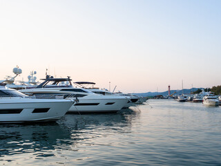 The yachts are moored in the calm sea and the silhouette of the mountains can be seen in the distance