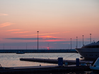 The bright setting sun hid behind the clouds above the sea pier. Pink sea sunset
