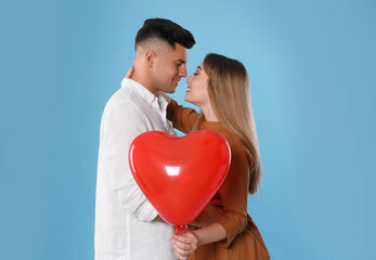 Fototapeta na wymiar Lovely couple with heart shaped balloon on light blue background. Valentine's day celebration