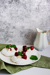 Meringue cakes decorated with whipped cream, cherries and mint leaves on a white plate, with a milk jug, side view with copy space