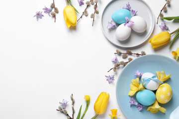 Festive Easter table setting with painted eggs and floral decor on white background, flat lay. Space for text
