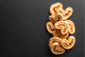 crispy puff pastry with sugar and cinnamon on a black stone background, top view, place for text