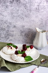 Meringue cakes decorated with whipped cream, cherries and mint leaves on a white plate, with a milk jug, side view with copy space