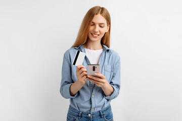 young woman holding credit card while using mobile phone on white background