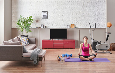 Sportive woman is doing yoga at home, purple mat, blue dumbbell, decorative living room concept. Healthy lifestyle.