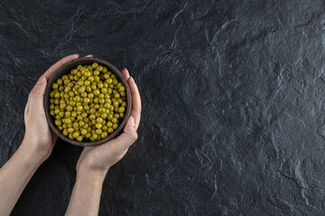Female holding bowl of marinated green olives on black background