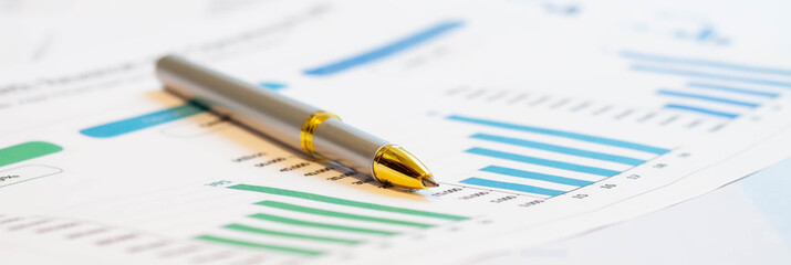 A silver pen with a gold tip rests on financial paper with a green chart