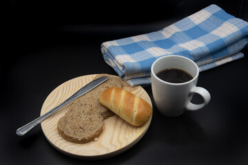 Una taza blanca con cafe, una  tostada de pan con un bollo de leche sobre un plato de madera y una...