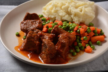 Spicy beef stew with smashed potatoes and boiled carrots and peas. Healthy food