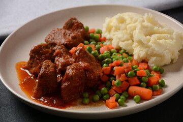 Spicy beef stew with smashed potatoes and boiled carrots and peas. Healthy food