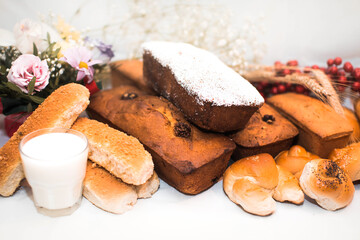 Buns of different types on a white tablecloth and a glass of milk
