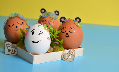 Easter eggs with funny faces in a box on a yellow-blue background. Easter.