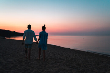 Silhouette of european couple holding each other hands and walking on the beach during sunset