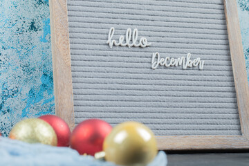 Hello december poster embedded on grey background with christmas balls aside