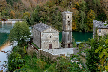 Fototapeta na wymiar The ancient Church of San Jacopo and behind the dam on the Lake of Isola Santa, Careggine, Italy