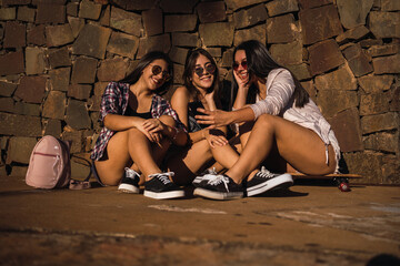 Three teenagers sharing online content on their smartphones sitting in a park.