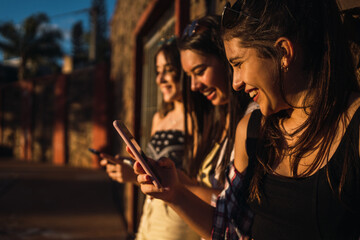 Obraz premium Three girls chatting with their smartphones at the park.