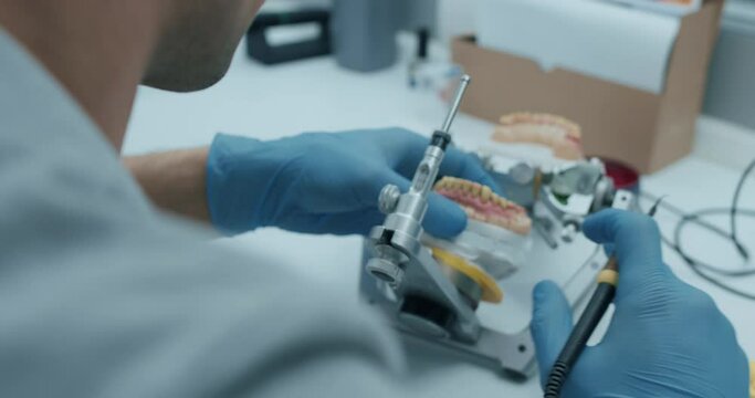 A male technician is holding a lower teeth model, putting it into a articulator yhen testing the dental prothesis working.