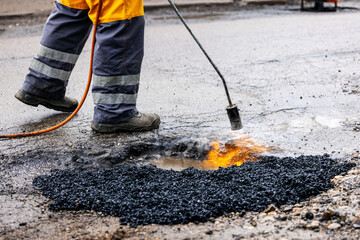 worker repairing pothole with bitumen on the road