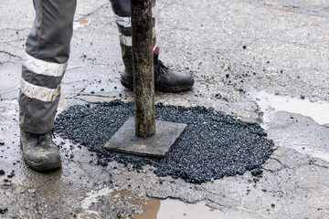 worker pushing bitumen in the hole. road repair and maintenance