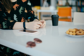 Women's hands on a table. a black cup of coffee, cookies and sunglasses
