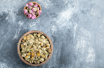 Wooden bowls of dried chamomile and rose on marble background