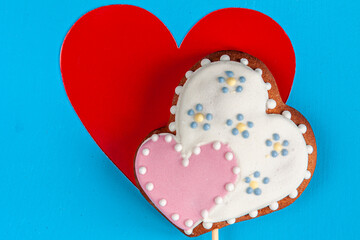 a red heart and a heart-shaped white and pink gingerbread on wooden stick on blue background