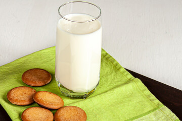 a tall glass of milk, cookies and a green towel on dark cutting board on white background