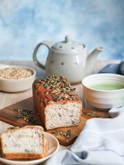 A healthy flour-less and multi grains  bread with a sliced piece on a wooden plate. With pot of tea and bowl of green tea matcha. A healthy and diet concept with a copy-space. 