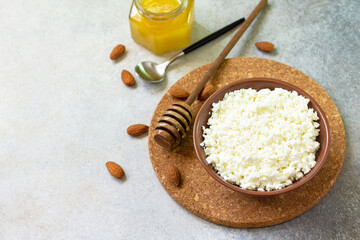Rich in calcium healthy food. Tvorog, farmers cheese, curd cheese or cottage cheese in a bowl with honey and almond on stone table. Copy space.