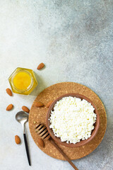 Rich in calcium healthy food. Tvorog, farmers cheese, curd cheese or cottage cheese in a bowl with honey and almond on stone table. Top view flat lay. Copy space.