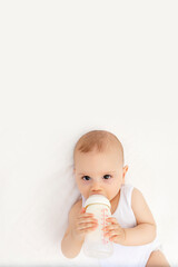 baby boy with a bottle of milk on a white bed at home, newborn baby drinks milk, baby food concept, place for text