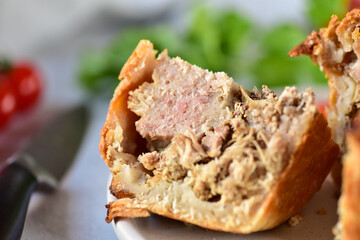 A slice of English pie with minced meat and meat, made from shortcrust pastry, lies on a gray plate, side view.