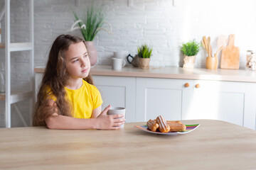 Obraz na płótnie Canvas cute school-age girl with curly-haired girls sits at a table in the kitchen, has fun, singing while waiting for food, a delighted child relaxes at the counter, enjoys a happy childhood at home 