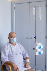 Fototapeta na wymiar Overweight man wearing a medical mask sits in a chair with a dropper, equipment in the foreground, patient in hospital, vertical photo
