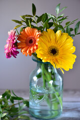 Pink, orange and yellow gerberas in a glass vintage vase, on a wooden table.